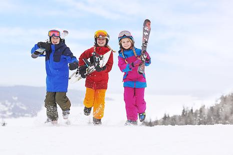 Drei Kinder tragen Ski und laufen durch den Schnee